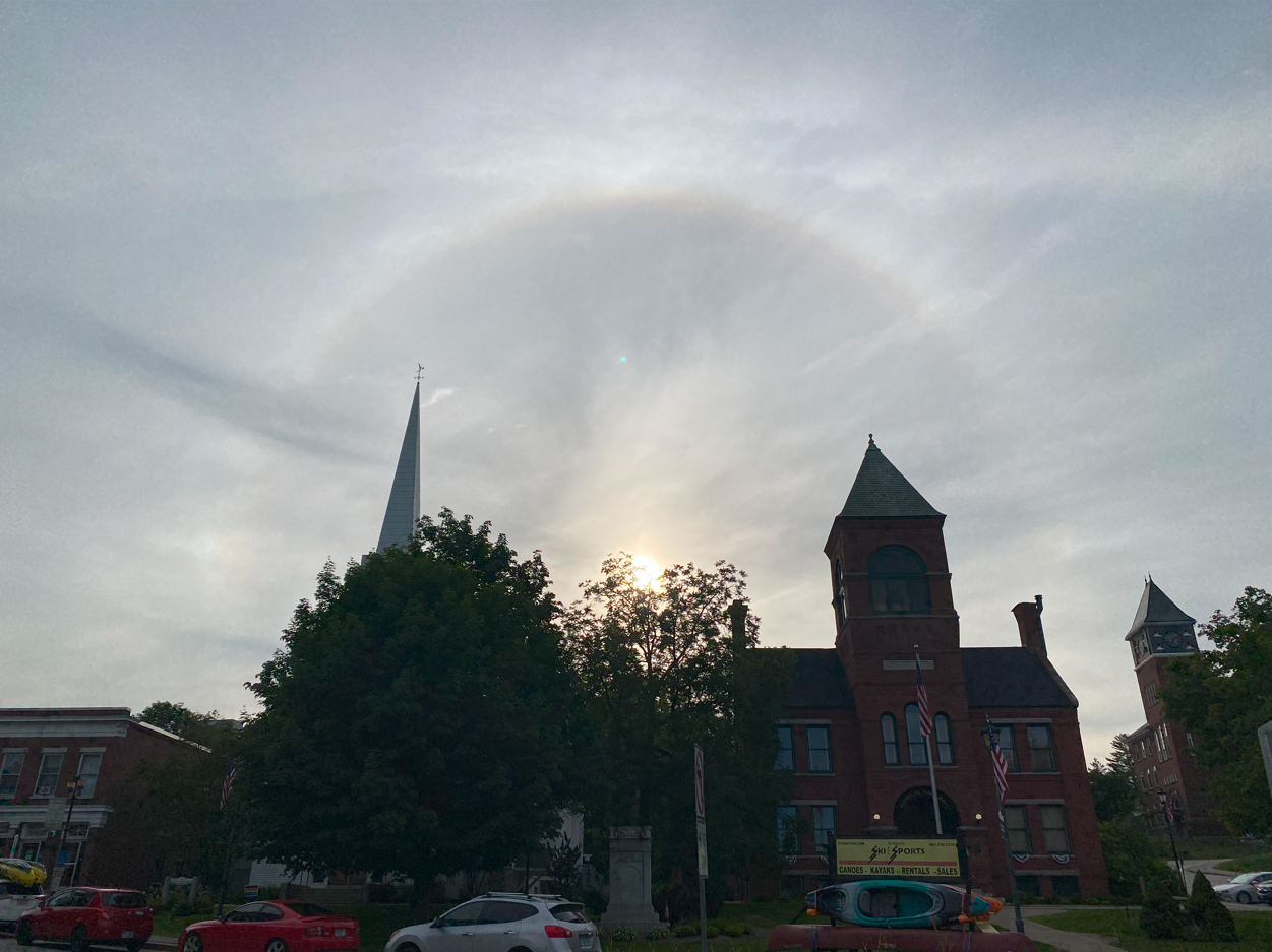 Early in the day we could see a sharp portion of a parhelic circle, a 120° parhelion (the brighter spot on the left of the first picture), and a faint parhelion (sundog) near a very sharp 22° halo. Sharp 22° halos like this one were visible for most of the day. The second picture, with the once again very bright 22° halo (and a hint of it being circumscribed) also shows a much fainter and somewhat broken parhelial circle with a radius similar to the 22° halo’s, coming out of the sun and more or less centered at the center of the picture. Parhelic circles become smaller and smaller as the sun is higher in the sky, but I had never had a chance to see anything like this, just little portions of low sun versions on a couple of occasions. The third picture is a clearer shot of the high sun and very bright circumscribed halo. Late in the day (next picture) the 22° halo was much fainter but a brightly colored circumzenithal arc (very high in the sky and circling the zenith) was clearly visible for a long time. The last picture shows the downtown shot in front of Town Hall that I had to take and for which I definitely did not park illegally.