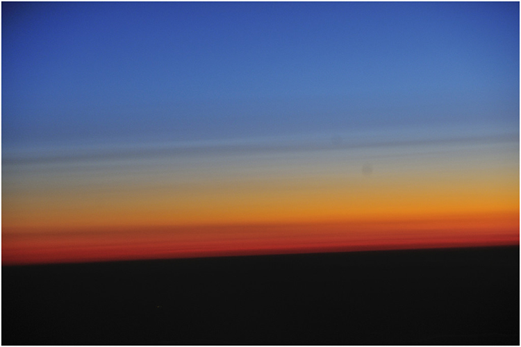 Picture of a sunset with blue sky and layers of yellow and red above a black horizon